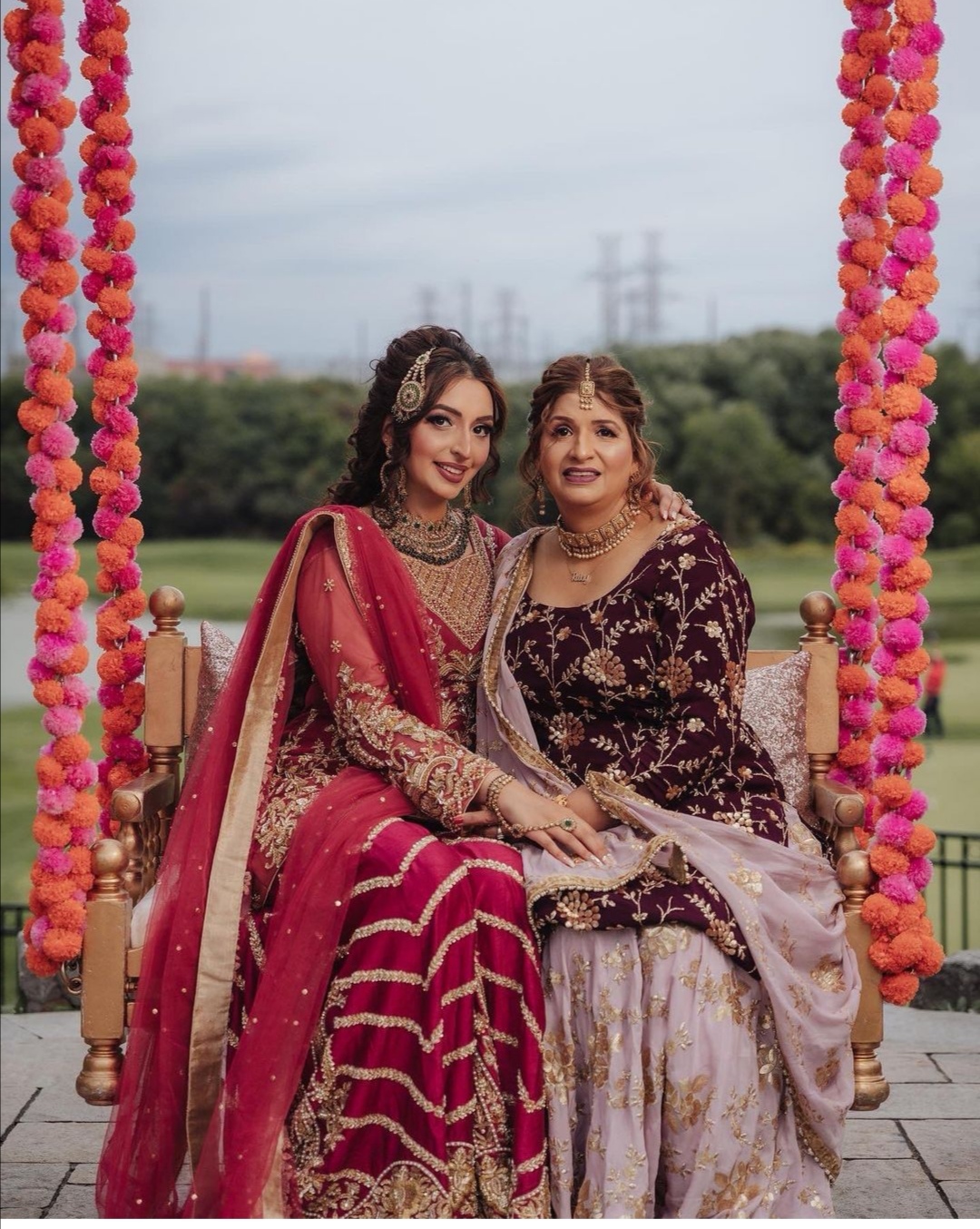 Real Sameera's Collection bride in crimson and gold with her mother in burgundy, on a marigold-draped swing